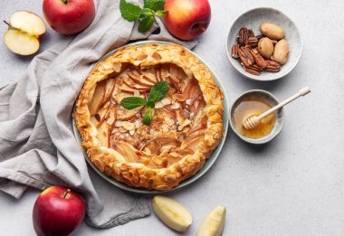 Badem yaprakları ve nane yapraklarıyla süslenmiş, bal ve fındıkla servis edilen açık yüzlü elmalı turta harika bir sonbahar ziyafeti sunuyor.