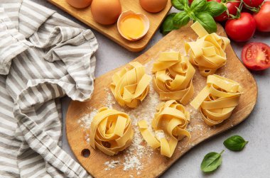 Tagliatelle makarna yuvaları pişmeyi bekliyor. Etrafı fesleğen, domates ve yumurtalarla çevrili.