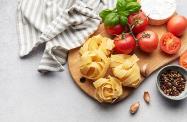 İtalyan makarna tagliatelle yuvaları domates, sarımsak, peynir ve fesleğen ahşap kesim tahtasının üzerinde dinleniyor.