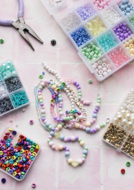 Renkli boncuklar, harf boncukları, ip, pense ve pense içeren el işi malzemeler pembe bir fayans yüzeyinde, mücevher yapımına hazır.