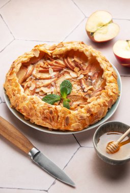 Badem gevreğiyle süslenmiş taze pişmiş elma galeti, yanında bal ve elma dilimleri, şık bir fayans masasında dinleniyor, tadını çıkarmaya hazır.