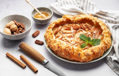 Badem taneli, tarçınlı ve naneli taze pişmiş elma galetesi. Etrafı malzemelerle ve mutfak malzemeleriyle çevrili.