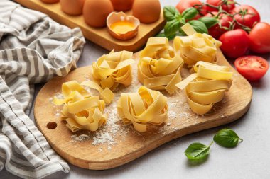 Tagliatelle makarna yuvaları pişmeyi bekliyor. Etrafı fesleğen, domates ve yumurtalarla çevrili.
