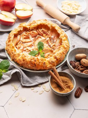 Badem taneli, tarçınlı ve naneli taze pişmiş elma galetesi. Etrafı malzemelerle ve mutfak malzemeleriyle çevrili.