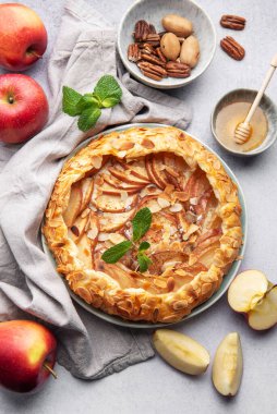 Badem yaprakları ve nane yapraklarıyla süslenmiş, bal ve fındıkla servis edilen açık yüzlü elmalı turta harika bir sonbahar ziyafeti sunuyor.