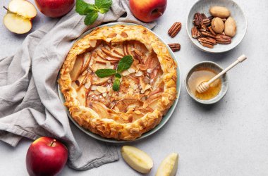 Badem yaprakları ve nane yapraklarıyla süslenmiş, bal ve fındıkla servis edilen açık yüzlü elmalı turta harika bir sonbahar ziyafeti sunuyor.