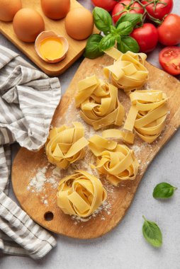 Tagliatelle makarna yuvaları pişmeyi bekliyor. Etrafı fesleğen, domates ve yumurtalarla çevrili.