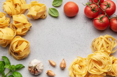 Tagliatelle yuvaları, sarımsak karanfilleri, domates ve fesleğen yaprakları mutfak masasında bir çerçeve oluşturur.