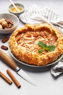 Badem taneli, tarçınlı ve naneli taze pişmiş elma galetesi. Etrafı malzemelerle ve mutfak malzemeleriyle çevrili.