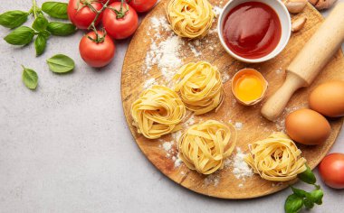 Tagliatelle ahşap tahtada malzemelerle dolu yuvaları İtalyan mutfak aşıkları için davetkar bir sahne yaratıyor.