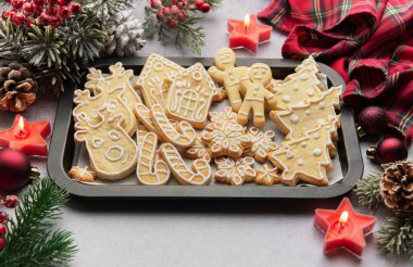 Noel kurabiyelerinin düz yatışı, kurabiye tepsisi üzerinde, etrafı şenlikli dekorasyonlar ve mumlarla çevrili, sıcak ve davetkar bir tatil sahnesi yaratıyor.