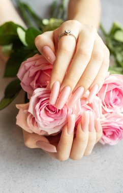 Pembe manikürlü bir kadının elleri pembe güller tutuyor ve elmas yüzüğünü gösteriyor.