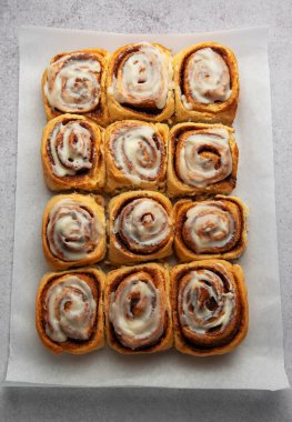 Taze pişmiş tarçınlı rulo, üzerine bol krem peynirli krema ile kaplanmış, pişirme kağıdında baştan çıkarıcı bir düzenleme oluşturur.