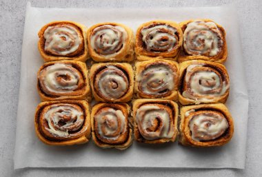 Taze pişmiş tarçınlı rulo krem peynirli krema, parşömen kağıdının üzerinde oturuyor.