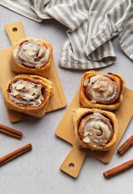 Taze pişmiş tarçınlı rulo, üzerine krema serpilmiş ve badem serpiştirilmiş, ahşap kesme tahtalarına oturmuş, eğlenmeye hazır.