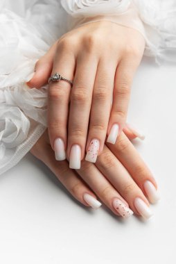 Beyaz arka planda beyaz tırnaklarını ve nişan yüzüğünü gösteren bir kadın.
