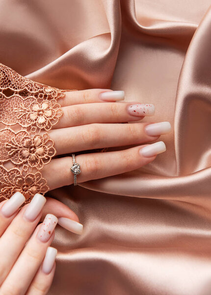 Женщина показывает стильные белые ногти с блестками и элегантное кольцо на шелковом фоне