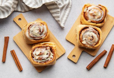 Taze pişmiş tarçınlı rulo, üzerine krema serpilmiş ve badem serpiştirilmiş, ahşap kesme tahtalarına oturmuş, eğlenmeye hazır.