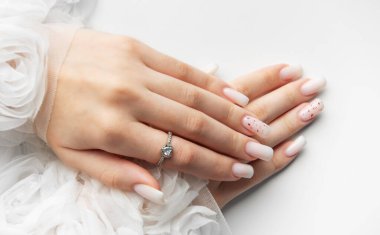 Beyaz arka planda beyaz tırnaklarını ve nişan yüzüğünü gösteren bir kadın.