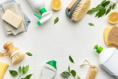 Beyaz fayans zemininde düzenlenmiş çevre dostu temizlik ürünleri, bulaşık fırçası, süngerler, sabun ve limon yarıları kopya alanı ile çerçeve oluşturma