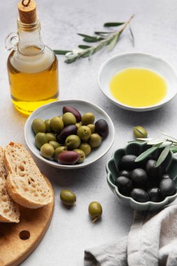 Mutfak masasında zeytin yağı şişesi, ekmek ve zeytin dalları bulunan yeşil ve siyah zeytinlerin üst görüntüsü