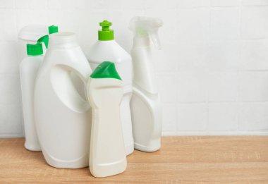 Temizleme sıvısı ve yeşil yapraklı beyaz plastik şişeler banyodaki ahşap rafta duruyor.