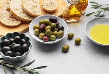 Akdeniz diyet malzemeleri arasında zeytin, zeytin yağı ve gri bir masaya yerleştirilmiş dilimlenmiş ekmek de var.