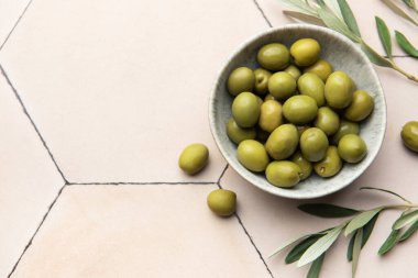 Yeşil zeytinler, fayanslı bir yüzeyde zeytin dallarıyla birlikte bir kasede servis edilir ve Akdeniz atmosferi oluşturur.