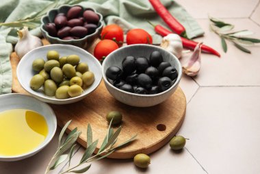 Kase dolusu siyah ve yeşil zeytin zeytin zeytinyağı, domates, sarımsak ve kırmızı biber ile ahşap bir tahtada düzenlenerek canlı bir mutfak sahnesi oluşturulur.