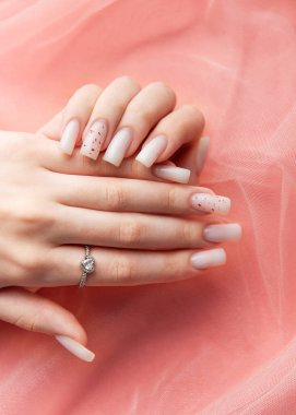 Kırmızı parıltılı beyaz manikürünü ve pembe arka planda nişan yüzüğünü gösteren bir kadın.
