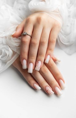 Beyaz arka planda beyaz tırnaklarını ve nişan yüzüğünü gösteren bir kadın.