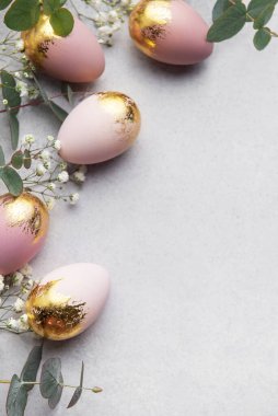 Altın yaprak ve okaliptüs yapraklarıyla süslenmiş pembe paskalya yumurtaları gri arka planda güzel bir sınır oluşturarak, kopyalama alanı bırakırlar.