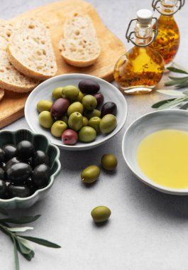 Akdeniz diyet malzemeleri arasında zeytin, zeytin yağı ve gri bir masaya yerleştirilmiş dilimlenmiş ekmek de var.