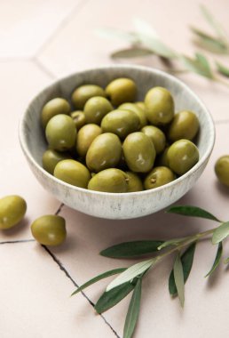 Yeşil zeytinler, fayanslı bir yüzeyde zeytin dallarıyla birlikte bir kasede servis edilir ve Akdeniz atmosferi oluşturur.