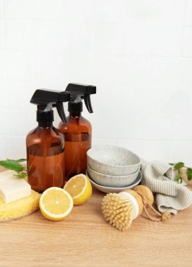 Doğal temizlik ürünleri, bulaşık fırçası, limon salonları, sünger ve kaseler ahşap tezgahta beyaz fayanslı duvara karşı dizilmiş.