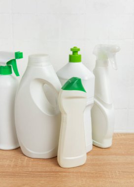 Beyaz fayansların önündeki tahta masanın üstünde duran plastik temizlik ürünleri ve deterjanlar.
