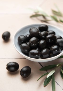 Zeytin dalıyla bej bir kapta siyah zeytin, Akdeniz mutfağı sahnesi yaratır.