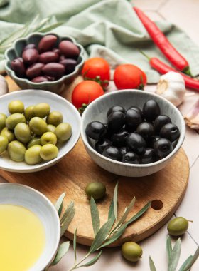 Mutfak masasında çeşitli zeytinler, domatesler, sarımsak, biber ve zeytinyağı, davetkar bir mutfak sahnesi yaratıyor.