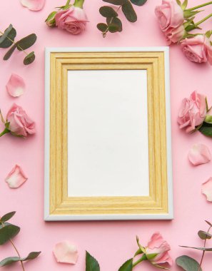 Pembe güller ve okaliptüs yapraklı ahşap çerçeve pembe arka planda romantik bir ortam yaratır. Sevgililer Günü projeleri için mükemmel.