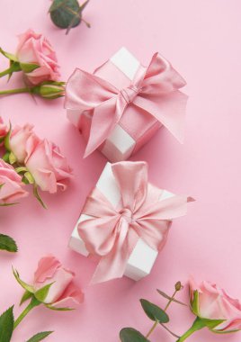 Pembe güllerin ve pembe arka planda saten kurdelelerin bulunduğu hediye kutularının şenlikli düzenlemeleri. Özel durumları kutlamak için mükemmel.