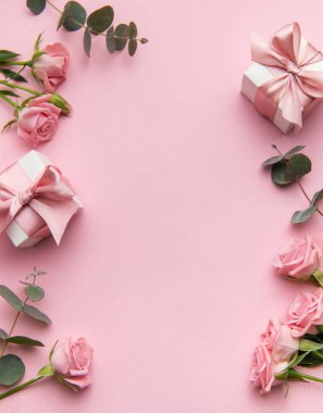 Pembe güller ve okaliptüs yaprakları pastel pembe bir fon üzerine dizilmiş.