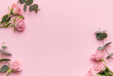 Pembe güller ve okaliptüs yaprakları pastel pembe bir fon üzerine dizilmiş.