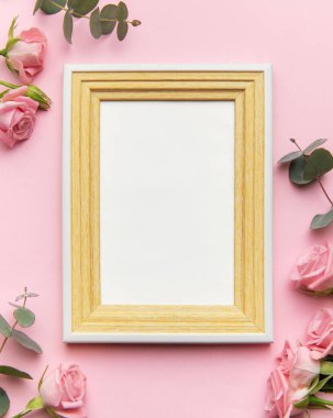 Ahşap çerçeve, pastel arka planda pembe güllerle çevrili.