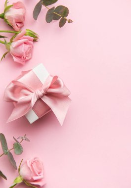 Pembe arka planda pembe kurdeleli ve güllü zarif hediye kutusu Sevgililer Günü veya Anneler Günü için romantik bir ortam yaratıyor.