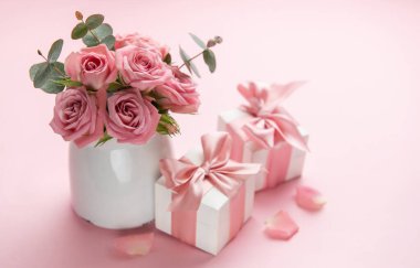 Beyaz vazoda pembe güller. Hediye kutuları, sevgililer günü için pembe kurdeleler, pembe arka planda anneler günü veya doğum günü.