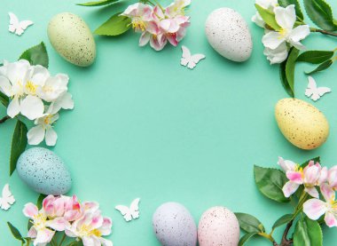 Bayramlık paskalya yumurtaları ve bahar çiçekleri turkuaz bir arka planda düzenlenerek güzel bir çerçeve oluşturuyor.