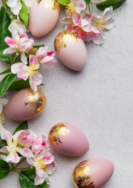 Altın folyo süslemeli ve bahar çiçekli zarif pembe paskalya yumurtaları gri arka planda güzel bir sınır oluşturur. Bayram kutlamaları için mükemmel.