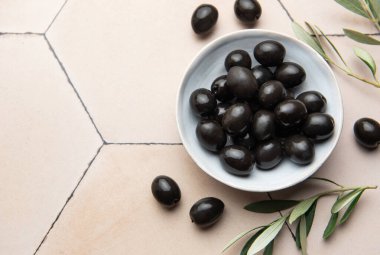 Zeytin dalıyla bej bir kapta siyah zeytin, Akdeniz mutfağı sahnesi yaratır.