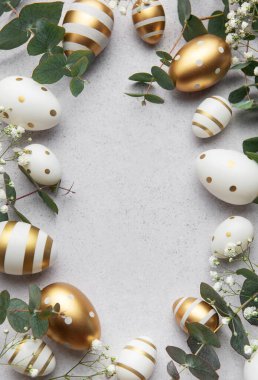 Paskalya yumurtaları okaliptüs yaprakları ve gri arka planda beyaz çiçeklerle bir çerçeve oluşturur.