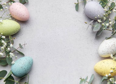 Pastel renkli paskalya yumurtaları ve okaliptüs yaprakları gri arkaplanda fotokopi alanı olan bir çerçeve oluşturuyor.